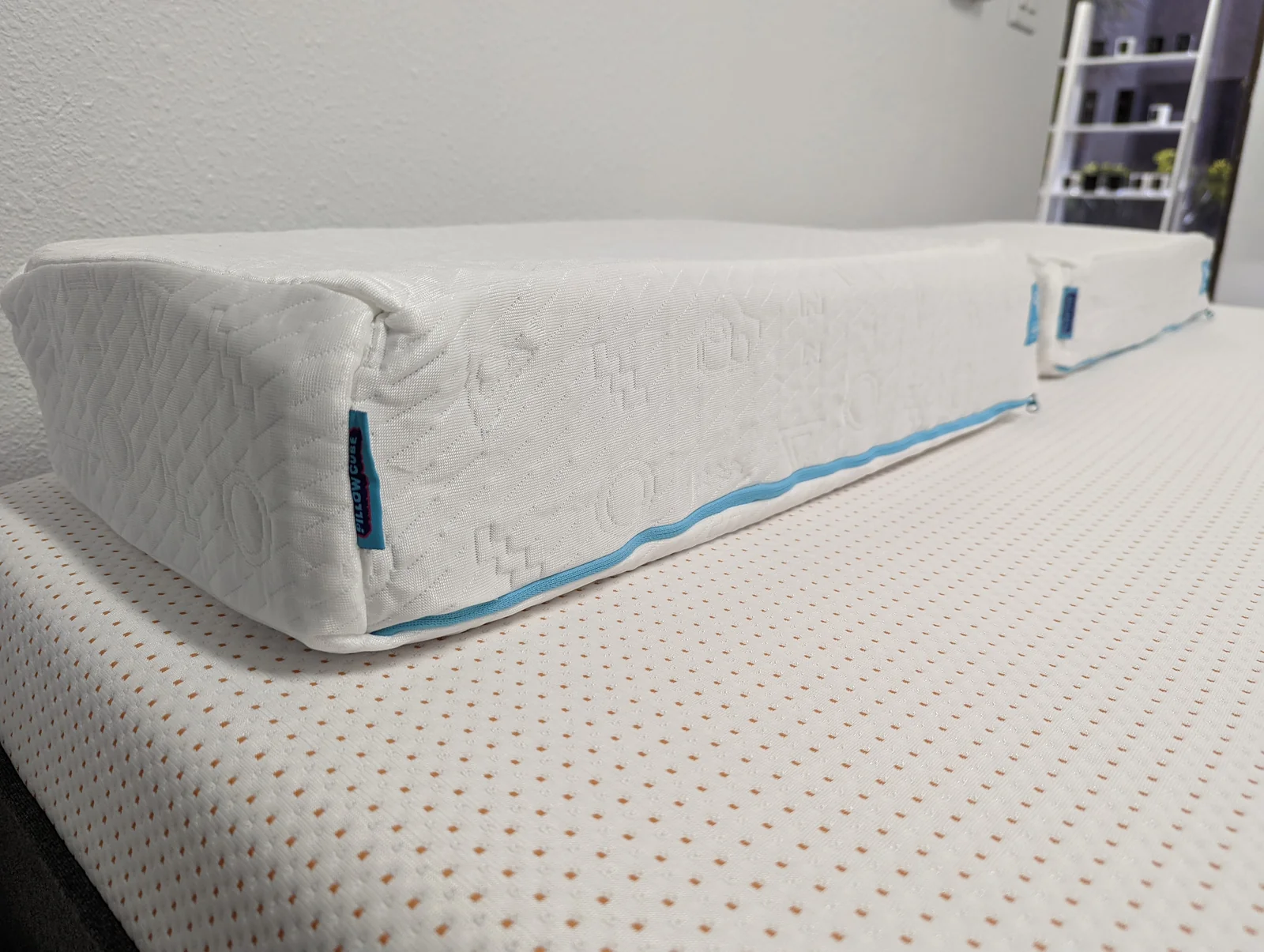 Archival photo showing the side profile and blue-trimmed zipper of a Pillow Cube Ice Cube on a mattress